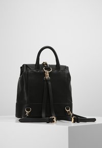 Czarny skórzany plecak o przemyślanej konstrukcji, zaokrąglonym górnym kształcie, podwójnych uchwytach, regulowanych paskach, złotych elementach metalowych i gładkiej teksturze.