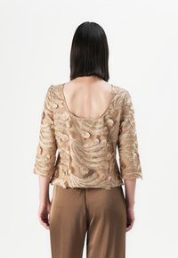 Beige bestickte Bluse mit dreiviertelärmel und abgerundetem Rückenausschnitt, die komplizierte federnartige Muster in strukturiertem Garn aufweist.