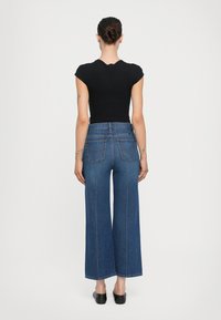 Top negro ajustado, vaqueros de mezclilla azules de pierna ancha y cintura alta, bolsillos estructurados, costuras azul claro, textura suave, dobladillo a la altura de la rodilla, combinado con zapatos negros.