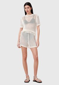 Hvid strikket mesh kortærmet top parret med matchende shorts, der har en løs pasform og tekstureret design. Sandaler med tynde stropper.