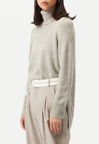 Ljusgrå polotröja i mjukt tyg med ribbade ärmslut, ihop med beige plisserade byxor och ett vitt bälte. Enkel, avslappnad design.