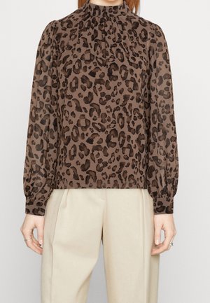 Blouse imprimé léopard marron avec un col haut, des manches longues et un détail froncé au niveau du col, associée à un pantalon beige.