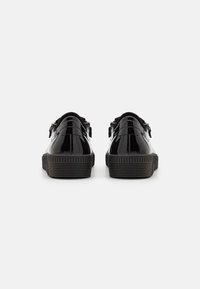 Scarpe in vernice nera con suola in gomma testurizzata, caratterizzate da una punta tonda e doppi dettagli a fibbia sul retro.
