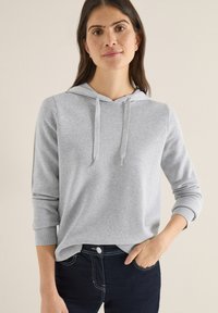 Felpa con cappuccio grigio chiaro con coulisse, maniche a tre quarti, polsini a costine e orlo leggermente curvo abbinata a jeans scuri.