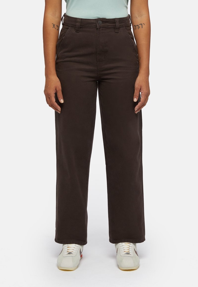 Pantalon large taille haute de couleur brun foncé, avec des poches avant et une texture lisse, associé à des baskets de couleur claire.