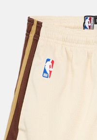 Bež košarkaške kratke hlače s smeđim bočnim panelima i zlatnom prugom. Sadrže NBA logo oznaku, izrađene od mrežastog materijala. Uključeni elastični pojas.
