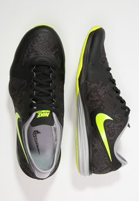 Černé sportovní boty s texturovaným povrchem, vybavené neonově žlutým „swoosh“, šedými stélkami a černými šňůrkami. Nízký střih s polstrovanou podrážkou.