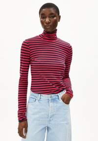 Gestreiftes Rollkragenoberteil in Rot und Marineblau, mit langen Ärmeln, aus weichem Stoff, getragen mit hellblauen hochtaillierten Jeans, Hände in den Taschen.