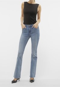 Mustaton hihaton toppi yhdistettynä vaaleansinisiin leveälahkeisiin farkkuihin. Farkuissa on klassinen viiden taskun muotoilu ja haalistunut pesu. Mustat teräväkärkiset korot.