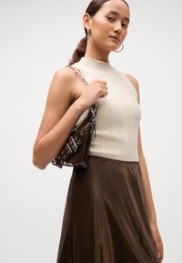 Sac à main en cuir verni marron avec une bandoulière en chaîne argentée, assorti à un haut sans manches en crème à côtes et à une jupe en satin marron. Textures lisses et design ajusté.