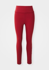 Rode hoge taille volle lengte leggings met zichtbare zijnaad en gedeeltelijk wit merkembleem op de onderkant van het rechterbeen tegen een witte achtergrond.