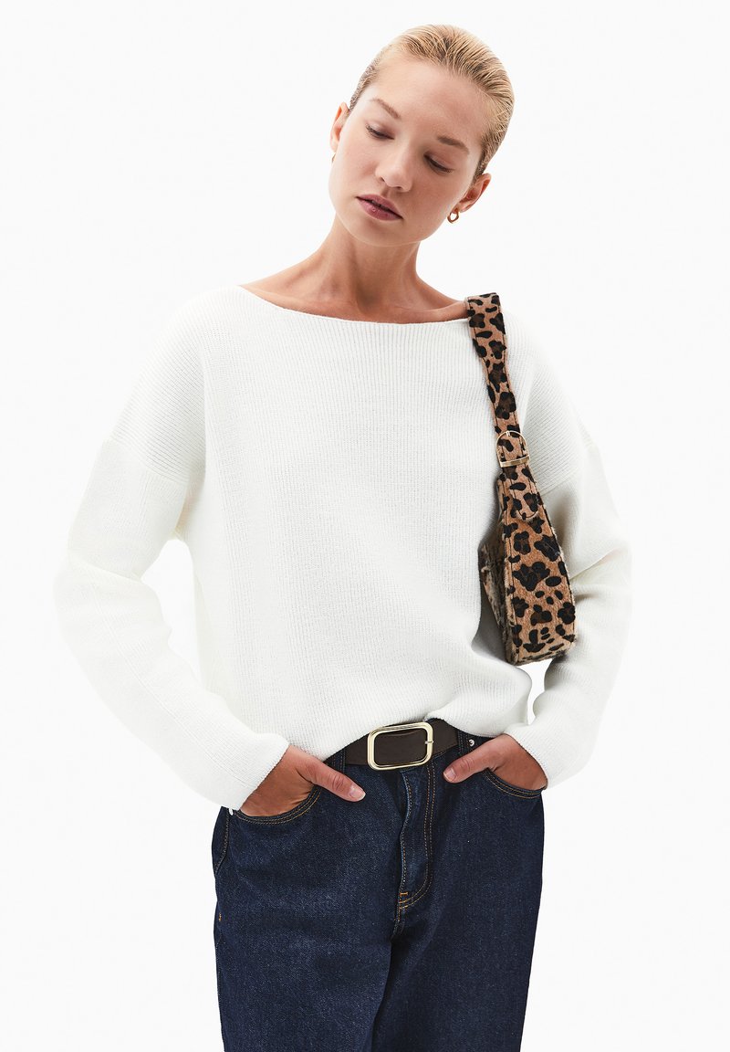 Biały sweter dziany z szerokim dekoltem, oversizedowe rękawy, zestawiony z ciemnoniebieskimi dżinsami i torebką o fakturze w leopardzie plamy.