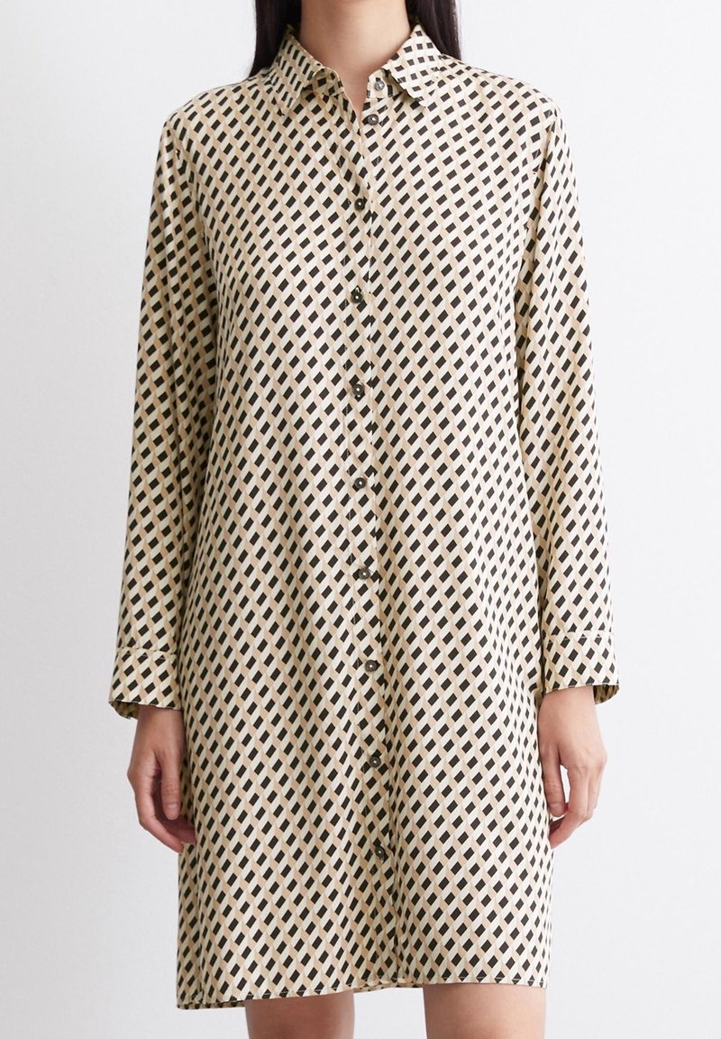 Robe chemise beige avec un motif à losanges noirs. Elle présente des manches longues et un col, fabriquée à partir d'un tissu léger.