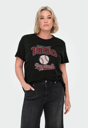 Blonde Frau in schwarzen Jeans trägt ein schwarzes T-Shirt mit "Chicago 1995 Baseball Club" und Baseball-Grafik, posiert mit einer Hand in der Tasche.