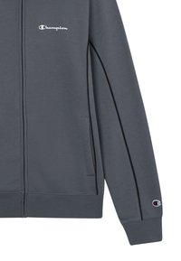 Grijze vest met ritssluiting, gemaakt van zachte stof, met het witte "Champion" logo op de borst, contrasterende zwarte zijstrepen en ribbels aan de mouwen.