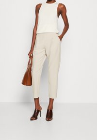 Beiga smalna byxor med sidofickor, kombinerat med en vit ärmlös topp. Bruna tåöppna klackmules och en brun handväska. Släta texturer.