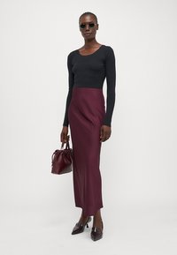 Top a maniche lunghe nero a coste abbinato a una gonna maxi in satin bordeaux fluida. Accessoriato con una piccola borsa bordeaux e scarpe con punta.