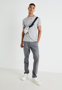Grå T-skjorte kombinert med grå bukser, komplementert av en sølvfarget midjeveske og hvite joggesko. Enkelt design og monokrom fargepalett.