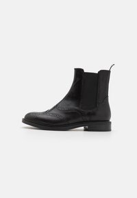 Botas Chelsea de couro preto apresentam um bico arredondado, detalhes em brogue, painéis laterais elásticos e um salto baixo em bloco para estabilidade.