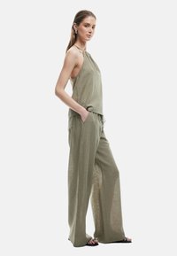 Top halter khaki con un ajuste relajado, combinado con pantalones de pierna ancha. Tela ligera, superficie texturizada y bolsillos laterales. Incluidas sandalias negras.