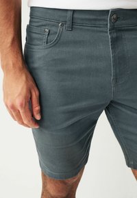 Szürke farmer rövidnadrág slim fit szabással, öt zsebes dizájnnal, látható varrással és fémből készült részletekkel a derékrészen.