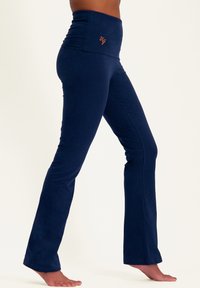 Dunkelblaue, ausgestellte Leggings mit hoher Taille und gerafftem Stoffdetail, das ein orangefarbenes Logoakzent an der Taille aufweist. Weiches, elastisches Material.