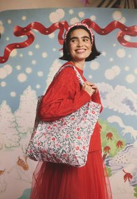 Rózsaszín virágmintás vászontáska, piros ajkakkal és zöld levelekkel díszítve. Anyaga textil, erős vállpántokkal.