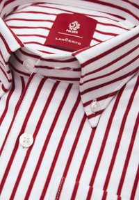 Koszula w czerwono-białe paski z kołnierzykiem zapinanym na guziki, z metką z tkaniny oznaczoną "LANCERT" oraz z przodem zapinanym na guziki.