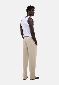 Pantalons en coton beige avec une taille élastique, présentés sur un modèle portant un débardeur blanc, vu de dos.