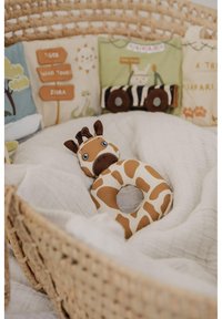 Giraffe-shaped teething toy in brown and cream, featuring large expressive eyes and a hollow center, resting on white fabric in a woven basket.