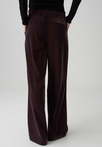 Burgundy, wide-leg trousers with a smooth texture, elastic waistband, and two back pockets. Simple design without embellishments.