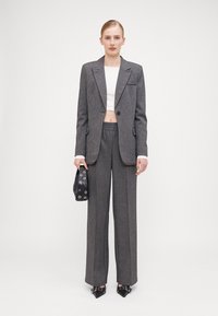 Szürke tweed öltöny, szabott blézerrel, széles nadrággal és fehér crop top-pal; kiegészítve egy fekete táskával, ezüst szemekkel és hegyes orrú cipőkkel.