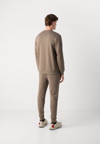 Completo da uomo in beige composto da felpa e pantaloni felpati, caratterizzato da una vestibilità rilassata, collo rotondo, polsini a costine e tessuto texturizzato, abbinato a sneaker beige.