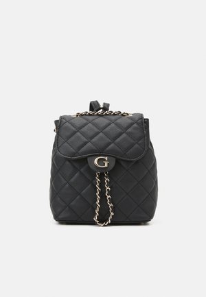 Sac à dos en cuir noir matelassé avec détail en chaîne dorée et fermeture à rabat ornée d'un emblème doré "G" sur fond blanc uni.