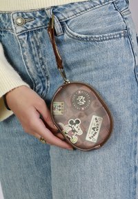Estuche marrón con cremallera y pegatinas retro de Mickey Mouse en la parte frontal, sujeto a un lazo para llaves, mostrado en una mano contra unos jeans de color azul claro.