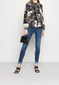 Blusa de manga larga con estampado multicolor, combinada con jeans ajustados azules. Bolso negro con acabado texturizado y tacones destalonados.