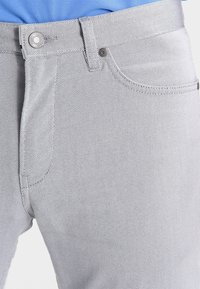 Ljusgrå denimjeans med en texturerad yta, femficksdesign, metallknappstängning och kontrasterande sömmar.