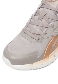 Šviesiai pilka sportinė avalynė su tekstūruotu tinklelio viršumi, metaliniu bronzos spalvos akcentu ir pagalvėle baltu padu, kontrastingai raišteliais.