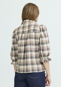 Kariertes Bluse in Beigetönen, Braun und Creme, mit gepufften Ärmeln, einem Rüschensaum und einem lockeren Schnitt. Aus weichem Flanellstoff.