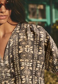 Haut à motifs floraux en tissu sombre avec des motifs botaniques blancs. L'encolure est en V, avec des manches amples et une texture douce.