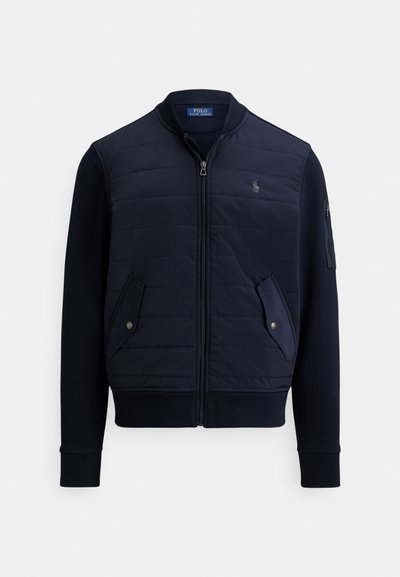 Πανωφόρι ναυτικού μπλε με φερμουάρ, με καπιτονέ εμπρός, ριμπ μανσέτες, δύο πλαϊνές τσέπες και λογότυπο στο στήθος. Διαθέτει ομαλή υφή υφάσματος.