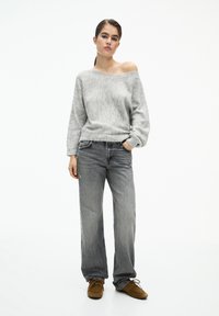 Maglione grigio chiaro, scollato sulle spalle, abbinato a jeans grigi larghi e strappati e sneakers marroni. Tessuto morbido, vestibilità casual, design minimale.
