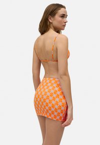 Bikini de color naranja con un patrón, con tirantes finos y una falda mini a juego, que presenta un diseño floral y una textura suave y elástica.