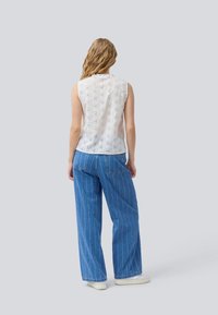 White, sleeveless blouse with a textured, embroidered pattern; paired with loose-fitting, blue, vertically striped denim jeans.