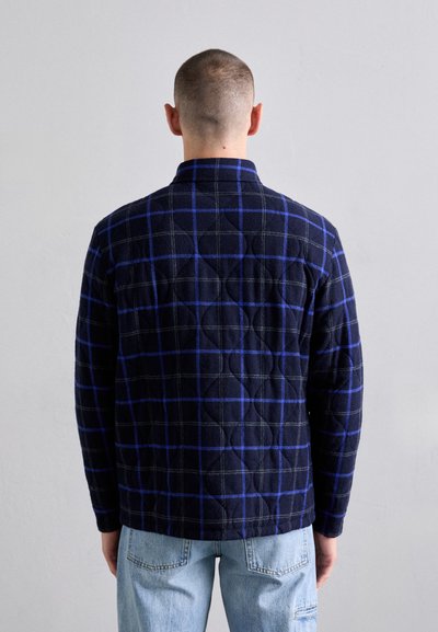Navy quilted flannel shirt with blue check pattern, featuring a collar and long sleeves. Back view shows textured detailing and a relaxed fit.
