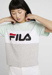 T-shirt à manches courtes en vert menthe, blanc et gris, avec un logo FILA noir et rouge bien en vue sur la poitrine ; en coton doux.