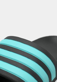 Zwarte glijderslipper met gestructureerde bandjes met twee turquoise strepen. Het ontwerp van de bandjes bevat horizontale lijnen voor visuele aantrekkingskracht.