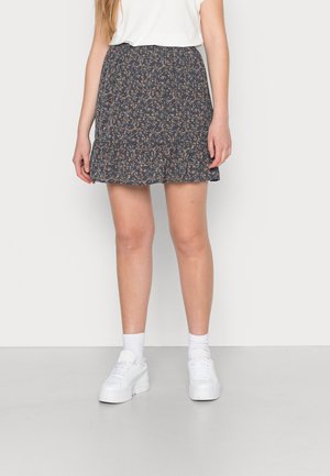 Saia azul-marinho com padrão floral e bainha em renda, feita de tecido leve, combinada com ténis brancos e meias cortas.