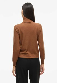 Brązowy sweter typu golf z dopasowanym krojem i ściągaczami, połączony z czarnymi spodniami o gładkiej teksturze dzianiny.
