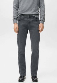 Vaqueros de mezclilla gris con corte de pierna recta, diseño de cinco bolsillos y sutil desgaste. Combinados con un suéter gris texturizado y zapatos negros.